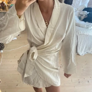 Vit omlottklänning - Säljer en stilren vit omlottklänning med knytband i midjan. Klänningen har långa ärmar och en elegant v-ringad design. Perfekt för en chic och avslappnad look.💓💓