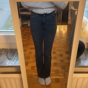 Svarta jeans med slits - Snygga svarta jeans med hög midja och slits vid anklarna. De har en klassisk straight passform och är perfekta för en stilren look. Jeansen har en dragkedja och knapp framtill.
