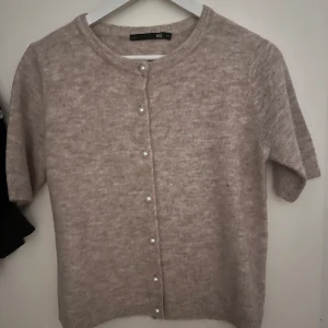Beige kofta med pärlknappar - Säljer en söt beige kofta från H&M med pärlknappar framtill. Koftan har korta ärmar och en rund halsringning. Perfekt för lager-på-lager under kyligare dagar. Från lager 157 storlek S använd 1 gång väldigt fint skick 