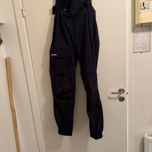 Svarta seglarbyxor från Tribord - Svarta seglarbyxor från Tribord Adventure, perfekta för segling. Byxorna har justerbara hängslen och elastiska benslut för en bekväm passform. Tillverkade i slitstarkt material med praktiska fickor. Nypris 1500 