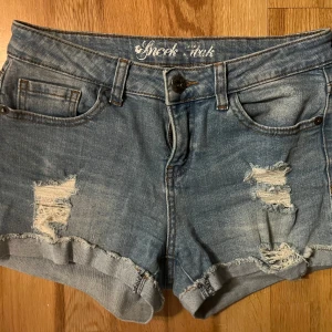 Blå jeansshorts med slitningar - Säljer ett par blå jeansshorts med slitna detaljer. Köpta i en second hand butik men säljer ingen för dem inte passade mig. Är aldrig använda av mig. 