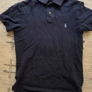 Svart pikétröja från Ralph Lauren - Säljer en klassisk svart pikétröja från Ralph Lauren. Tröjan har korta ärmar och en broderad logotyp på bröstet. Perfekt för en stilren och avslappnad look. Skickt 7/10