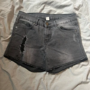Grå jeansshorts med slitningar - Snygga grå jeansshorts med coola slitningar på framsidan. De har en klassisk femficksdesign och knappgylf. Perfekta för en avslappnad stil.