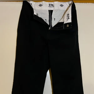 dickies 874 original fit - Säljer ett par klassiska svarta byxor från Dickies, modell 874. Byxorna har en rak passform och är tillverkade i slitstarkt material. De har en dragkedja och knapp framtill samt Dickies-logga på baksidan. Perfekta för en stilren look. (Aldrig använda) Nypris:799 Priset är inte hugget i sten