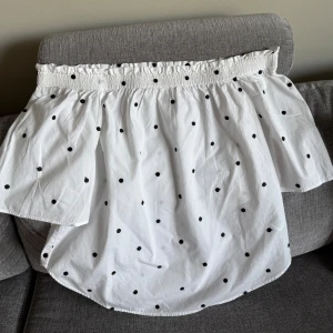 Snygg H&M vit blus, storlek 36. Ny - Vit off-shoulder blus med svarta prickar och resår vid halsen. Blusen har korta, vida ärmar. Aldrig använd, bara tvättad. Kommer från djur&rökfritt hem. 