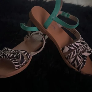 Zebramönstrade sandaler med turkosa remmar - Snygga sandaler med zebramönster och turkosa remmar. Perfekta för en somrig look med en unik touch. Sandalerna har en öppen tå och justerbara remmar för bästa passform.