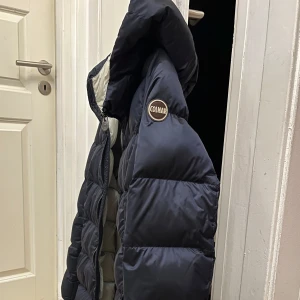 Mörkblå dunjacka Colmar - Säljer min snygga dunjacka från Colmar. Jackan har en lång modell med huva och dragkedja framtill. Perfekt för kyliga dagar med sin vadderad insida som håller dig varm. Storlek M använd ett par gånger. Lite sminkfläckar på insidan av huvan som är lätt att tvätta bort💙