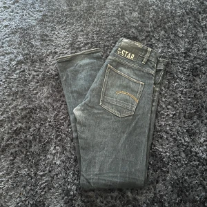 Svarta jeans från G-Star - Snygga svarta jeans från G-Star med klassisk femficksdesign och subtila gula sömmar på bakfickorna. Jeansen har en rak passform och är perfekta för en stilren look. Märkeslogga synlig på baksidan och vid fickan.