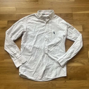 Ralph lauren skjorta - Klassisk vit skjorta från Polo Ralph Lauren i storlek S. Skjortan har button-down krage, lång ärm och broderad logga på bröstet. Tillverkad i bomull med snygg passform och knappar framtill. Perfekt för en clean och stilren look.