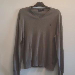 Grå v-ringad tröja Polo Ralph Lauren - Snygg grå v-ringad tröja från Polo Ralph Lauren i mjuk pima bomull. Klassisk design med broderad logga på bröstet och långa ärmar. Köparen betalar frakten