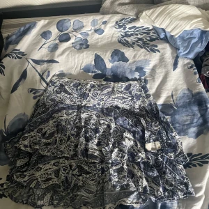 Blåvit mönstrad kjol Odd Molly - Supersöt kort kjol från Odd Molly i blått och vitt med paisleyinspirerat mönster. Kjolen har volangdetaljer och är tillverkad i ett lätt och luftigt material.