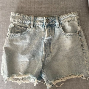 Jeansshorts - Ljusblå jeansshorts med hög midja och slitning. Storlek 36.