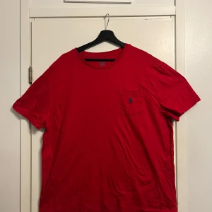 Röd t-shirt från Polo Ralph Lauren XL - Riktigt snygg röd t-shirt från Polo Ralph Lauren i klassisk passform. T-shirten har korta ärmar, rund halsringning och en bröstficka med den ikoniska blå broderade loggan. Tillverkad i 100% bomull för skön känsla hela dagen.