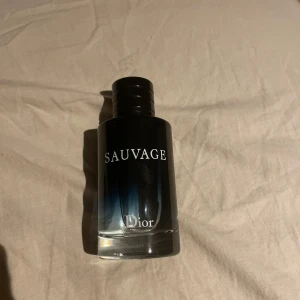 Dior Sauvage Eau de Toilette - Dior Sauvage parfym i en stilren glasflaska med svart till blå toning och silverdetaljer. Flaskan har tydlig Sauvage-logga framtill och CD-logga på locket. En ikonisk doft med maskulin och fräsch känsla, perfekt för dig som gillar exklusiva parfymer.