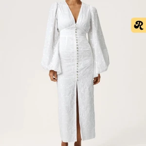 Vit långklänning från Adoore - Superfin vit långklänning från Adoore med v-ringning, långa puffärmar och knappar framtill. Klänningen har broderade blommor i tyget och en slits framtill för extra vibe. 