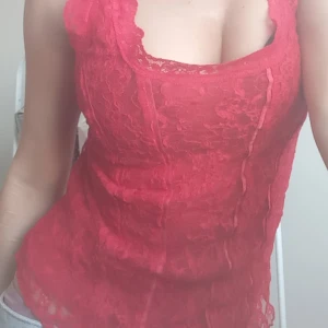 Röd spetsig linnetopp - Säljer en röd ärmlös linnetopp i spets med snygg fyrkantig ringning och genombrutet mönster. Toppen har figurnära passform och fina vågiga kanter vid axlar och nederkant. Perfekt att styla med jeans eller kjol för en trendig look.