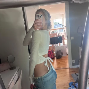 Vit ribbad croppad topp med knyt - Säljer en vit långärmad croppad topp med ribbad struktur och snygg knytning i ryggen. Toppen har en tight passform och är perfekt för dig som gillar trendiga detaljer och öppen rygg. Superfin att styla med jeans eller kjol.