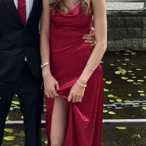 Röd långklänning med öppen rygg - Säljer en elegant röd långklänning i satinliknande material med smala axelband, öppen rygg och snörning. Klänningen har en snygg slits framtill och en figurnära passform som ger en lyxig känsla. Perfekt för bal eller student! Har bara använt en gång!!❤️orginal pris 1300kr