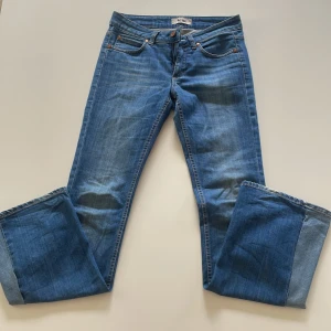 Blå bootcut jeans från Acne - Säljer ett par klassiska blå bootcut jeans från Acne med låg midja. Jeansen har fem fickor, snygg tvätt och Acne-läderpatch bak i midjan. Perfekt passform med lite utsvängda ben. Materialet är mjukt denim i bomull.