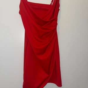 Röd klänning - Snygg röd kortklänning med smala axelband och draperad framsida. Klänningen har en rak passform och är tillverkad i ett mjukt, stretchigt material som sitter bekvämt. Perfekt för dig som vill sticka ut med en enkel men effektfull look. Sitter jättebra på kroppen ☺️passar S &xs då den är strechig!