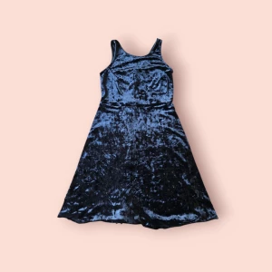 Svart sammetklänning från Ofelia - Supersnygg svart sammetklänning från Ofelia med ärmlös design och lätt utställd kjol. Klänningen har en glansig yta som ger en lyxig känsla och passar perfekt när du vill sticka ut lite extra. Enkel men ändå elegant look.