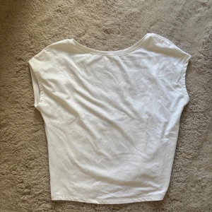 Vit ärmlös topp med rund hals och en djup rygg - En basic vit topp i mjuk bomull med rundad halsringning fram och djupare urringning bak. Modellen är ärmlös och har en rak, avslappnad passform som passar perfekt till jeans eller kjol. Enkel och stilren design som funkar året runt.