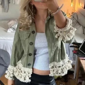 Grön jacka från Zara med virkade detaljer - Snygg ljusgrön jacka från Zara med virkade, beige volangdetaljer och tofsar längs ärmslut och nederkant. Jackan har stora bröstfickor, knappar framtill och en croppad passform. Perfekt för dig som vill sticka ut med en unik och trendig look.