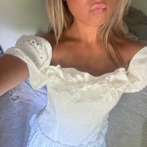 Vit offshoulder klänning med volang - Superfin vit kortklänning med offshoulder och volangdetaljer. Klänningen har broderade mönster. Fint skick 