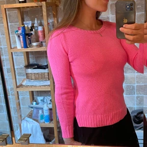Rosa stickad tröja med rund hals - Säljer en snygg rosa stickad tröja med rund halsringning och ribbade muddar vid ärmslut och nederkant. Tröjan har lång ärm och en klassisk, enkel design som är lätt att matcha till olika outfits.