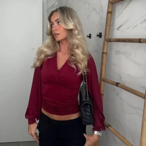 Vinröd omlottopp med v-ringning - Snygg vinröd omlottopp från Nelly med v-ringning och långa puffiga ärmar. Toppen är croppad och har rynkade detaljer i sidorna.