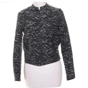 Moto jacket med mönster stl 36 - Snygg svartvit bomberjacka med grafiskt mönster och dragkedja framtill. Tjockt tyg som håller formen och inte blir skrynkligt. Jackan har lång ärm, rundad hals och två fickor med dragkedja. Perfekt för dig som gillar en modern och stilren look.