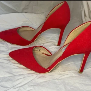 Röda pumps från NLY Shoes, storlek 36 - Snygga röda pumps från NLY Shoes med spetsig tå och hög klack. Skorna är i mockaimitation och har en stilren, öppen design på sidorna. Perfekta för dig som vill sticka ut med färg och elegans.