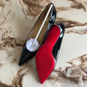 Svarta Louboutin pumps med röd sula - Klassiska svarta pumps från Christian Louboutin i lackat skinn med ikonisk röd sula. Skorna har spetsig tå och smal klack, perfekt för dig som vill sticka ut med en elegant och tidlös look.