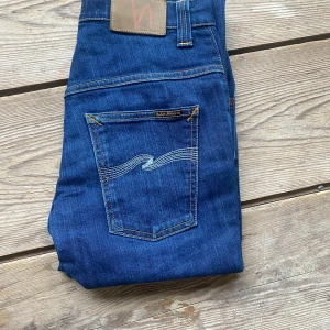 Blå jeans från Nudie Jeans Co - Snygga blå jeans från Nudie Jeans Co med klassisk femficksdesign och kontrastsömmar. Bakfickorna har Nudies ikoniska broderi och ett brunt läderpatch med logga. Jeansen har normal passform och är tillverkade i slitstarkt denim.