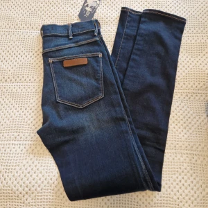 Wrangler jeans W28 L32 - Helt nya snygga jeans från Wrangler med klassiska kontrastsömmar och läderpatch på bakfickan. Modellen heter Jess och har en smal passform med normal midja. Tillverkade i stretchig bomullsdenim för en bekväm känsla. Köptes på rea för 800kr. men storleken var ju helt fel för mig.
