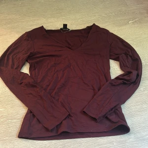 Vinröd långärmad tröja från Amisu - Säljer en vinröd långärmad tröja från Amisu i storlek M. Tröjan har en snygg v-ringning och är tillverkad i mjukt bomullsmaterial. Perfekt för dig som gillar enkel och stilren design med en djupare färgton.