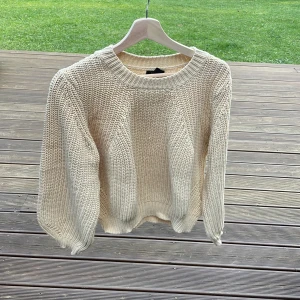 Beige stickad tröja med grov struktur - Säljer en beige stickad tröja med grov struktur och rund halsringning. Tröjan har långa ärmar och ribbade muddar vid ärmslut och nederkant. Perfekt för lager-på-lager och chill höst- eller vinterstil.