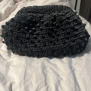 Svart pärlstickad handväska - Säljer en svart handväska med stickad struktur och dekorerad med små svarta pärlor. Väskan har en rektangulär form och stängs med ett metallspänne upptill. Perfekt accessoar för att lyfta din outfit. Från Lindex köpt för 599