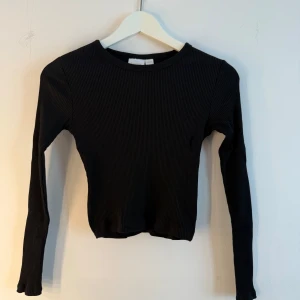 Svart ribbad långärmad topp Gina Tricot - En svart, ribbad långärmad topp från Gina Tricot. Modellen är figurnära med rund halsringning och stretchigt material som sitter snyggt på kroppen. Perfekt att styla med jeans eller kjol för en clean look. Storlek 164/som en XS