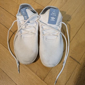 Adidas Pharrell Williams Hu vita sneakers - Snygga Adidas Pharrell Williams Hu sneakers i vitt med ljusblå detaljer på plös och häl. Ovandel i mesh för en luftig känsla och cool look. De är lite smutsiga och de har fläckar. Du kanske kan få de rena och fina igen. I använt bra skick. Storlek 38 2/3.
