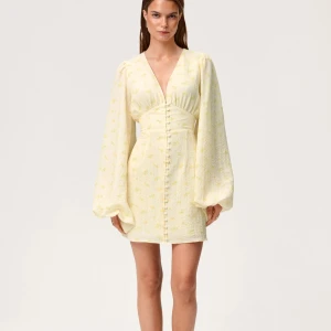 Adoore Florence kort klänning gul - Supersöt kort klänning från Adoore i ljusgul nyans med små blommor. Djup v-ringning, markerad midja och långa puffärmar. Klänningen har knappar framtill och är tillverkad i ett strukturerat tyg som känns lyxigt och somrigt. Alla prislappar kvar. Endast intressekoll då jag inte vet om de är värt att sälja 