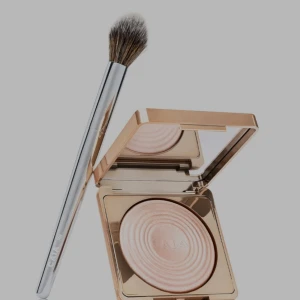 CAIA highlighter med borste - Lyxig highlighter från CAIA i en snygg guldig förpackning med spegel. Pudret har en ljus champagnefärg med skimrande finish. Medföljer gör en fluffig sminkborste med silverfärgat skaft, perfekt för applicering av highlighter.
