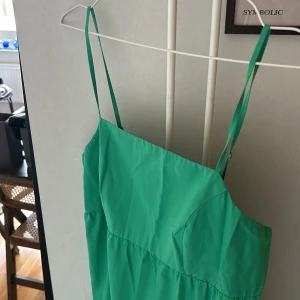 Grön ärmlös långklänning - Snygg grön långklänning med tunna axelband och volangdetaljer. Klänningen har en enkel, luftig design som passar perfekt för varma dagar. 