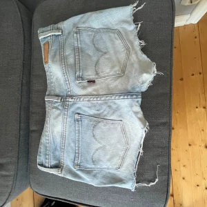  Lågmidjade Levi's jeansshorts - Säljer ett par ljusblå jeansshorts från Levi's med råa, fransiga kanter och klassiska bakfickor. Shortsen har låg midja och en avslappnad passform. Perfekta för sommardagar och festivaler. Snygg slitning och klassisk Levi's-detalj på bakfickan. Tar emot prisförslag❤️