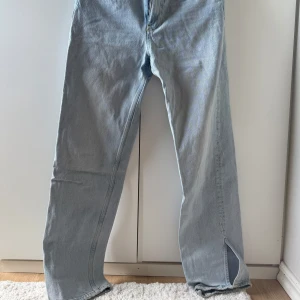 Ljusblå jeans med slits  - Säljer ett par ljusblå raka jeans från Gina tricot perfect jeans. De har klassisk femficksdesign, normal midja och snygga slitsar nertill på benen. Jeansen är i denim och har dragkedja och knapp framtill. Perfekta för en chill och trendig look.