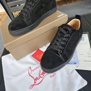 Svarta sneakers från Christian Louboutin - Snygga svarta sneakers i mocka från Christian Louboutin med klassisk röd sula och svarta skosnören. Skorna har rund tå, platt sula och lyxig beige insida i skinn. Perfekta för dig som vill sticka ut med exklusiv streetstyle.