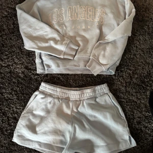 Ljusgrå sweatshirt från Pigalle - Säljer en ljusgrå sweatshirt från Pigalle med texten 'Los Angeles California' framtill. Tröjan har rund hals, långa ärmar och ribbade muddar. Perfekt för en avslappnad stil och enkel att matcha med andra plagg. Även shortsen ingår! Tröjan är i storlek Xs och shortsen M