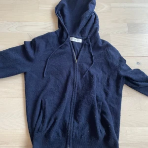 Kashmir zip - Mörkblå Kashmir hoodie från Zadolo med dragkedja framtill och huva med snörning. Tröjan har långa ärmar och två fickor framtill. Tröjan är lite nopprig men annars i ett hyfsat skick. Tröjan är i storlek XS alltså Zadolos xs.