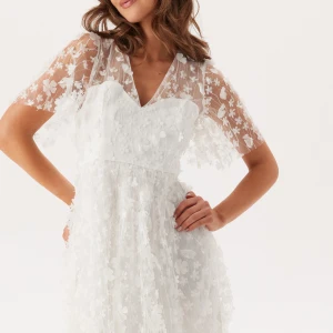 Studentklänning - Vit blommig chiffongklänning - Superfin vit klänning i chiffong med blommiga 3D-detaljer och v-ringning. Klänningen har korta ärmar i transparent tyg och en romantisk känsla. Perfekt för sommarens speciella tillfällen eller studentfirande. Oanvänd! Ordinarie pris 999kr