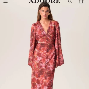 Blommig långklänning med v-ringning och vida ärmar från Adoore - Säljer min klänning från Adoore i rödrosa toner med blommigt mönster. Klänningen har endast använts en gång